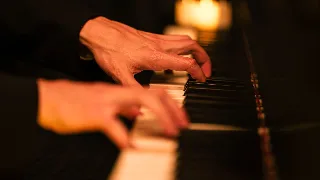 Dłonie pianisty na klawiaturze, obok płonąca świeca